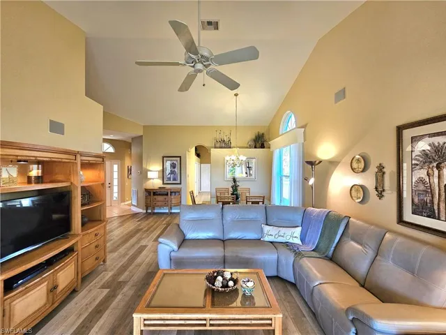 Living room with ceiling fan with notable chandelier, hardwood / wood-style floors, and high vaulted ceiling