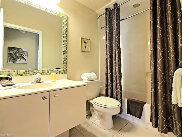 Full bathroom with tile patterned floors, toilet, vanity, shower / bath combo with shower curtain, and decorative backsplash