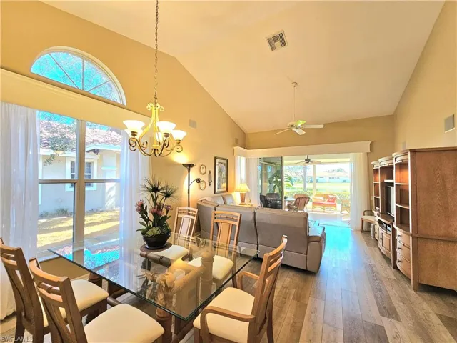 Dining space featuring hardwood / wood-style flooring, ceiling fan with notable chandelier, and high vaulted ceiling
