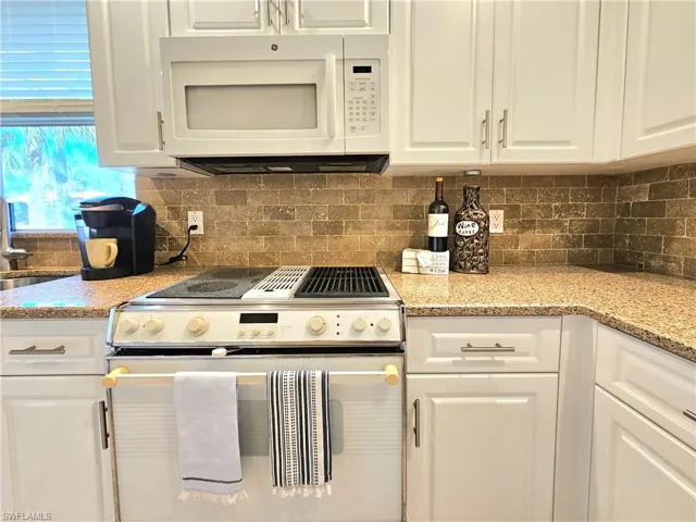 Kitchen with backsplash, white cabinets, white appliances, and light stone counters