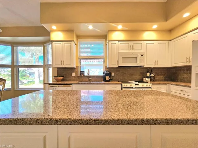 Kitchen with white cabinetry, sink, white appliances, and a kitchen island