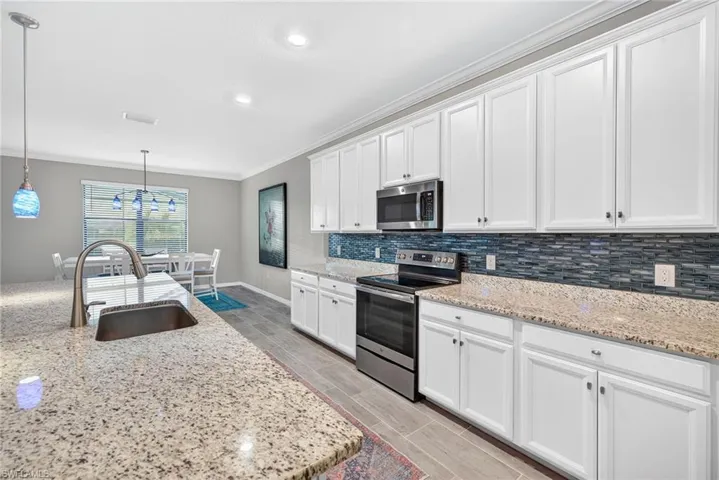 Kitchen with stainless steel appliances, crown molding, hanging light fixtures, light stone counters, and white cabinetry