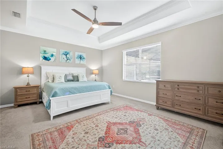 Carpeted bedroom featuring a raised ceiling, crown molding, and ceiling fan