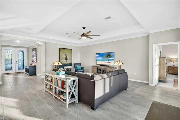 Living room with arched walkways, a tray ceiling, ornamental molding, french doors, and a ceiling fan
