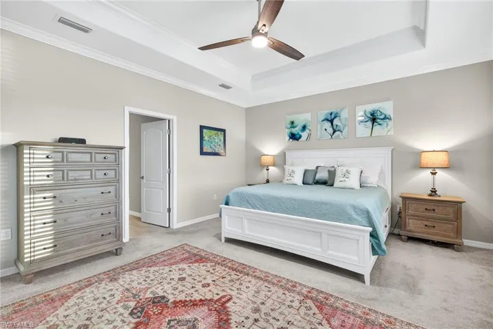 Bedroom featuring light carpet, ceiling fan, a tray ceiling, and crown molding