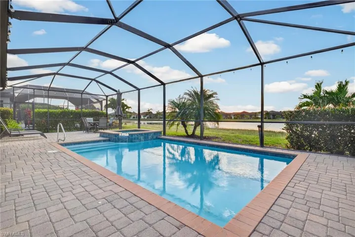 View of swimming pool featuring a sunroom, glass enclosure, a pool with connected hot tub, a water view, and a patio