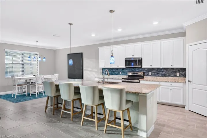 Kitchen with ornamental molding, a breakfast bar area, white cabinets, appliances with stainless steel finishes, and decorative light fixtures