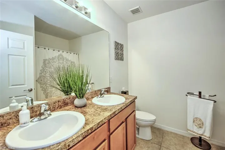 Bathroom featuring toilet, tile patterned flooring, and dual bowl vanity
