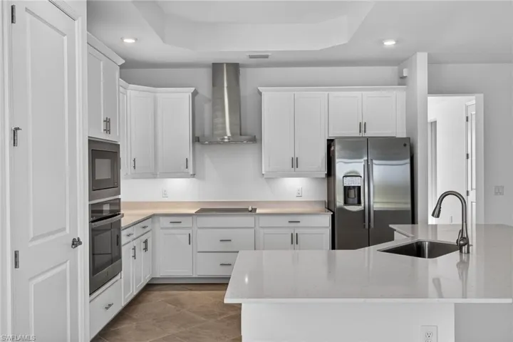 Kitchen with black appliances, recessed lighting, white cabinets, light stone countertops, and a tray ceiling