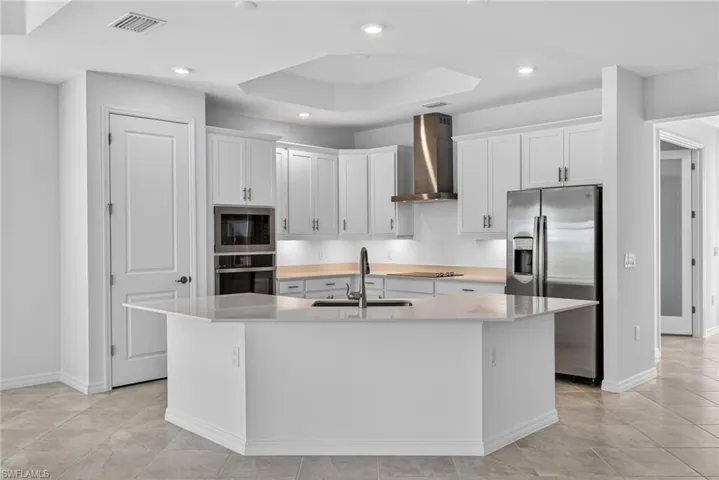 Kitchen featuring white cabinets, stainless steel appliances, a center island with sink, light stone counters, and recessed lighting