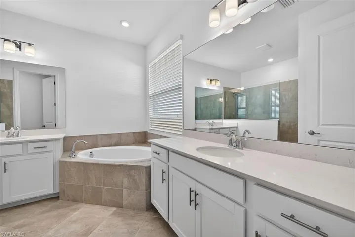 Primary Bathroom featuring a bath, two vanities, a walk in shower, and recessed lighting
