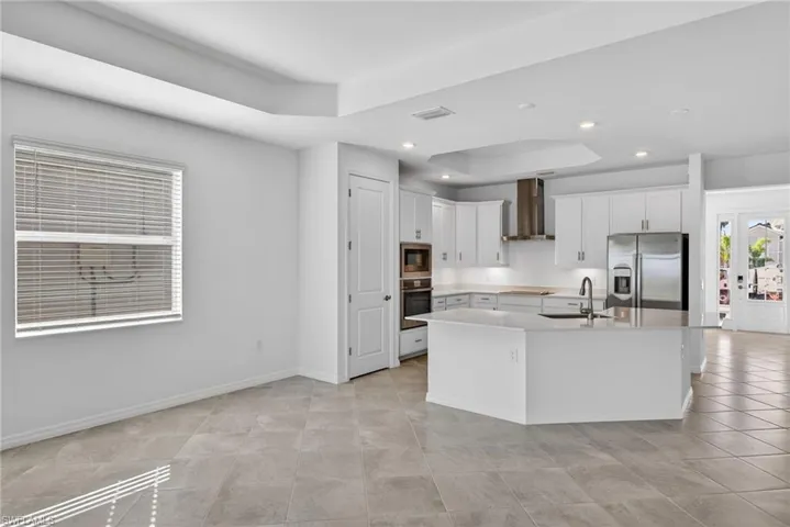Kitchen featuring white cabinetry, stainless steel appliances, a raised ceiling, a kitchen island with sink, and french doors