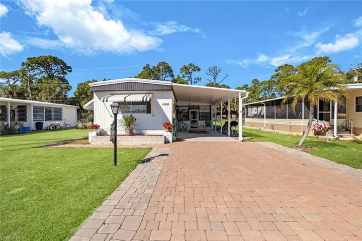 View of front of home featuring a front lawn, an attached carport, decorative driveway, and a sunroom