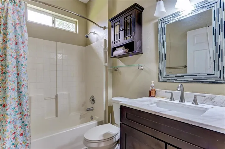 Bathroom featuring a dark wood vanity with a white countertop and rectangular sink, a white tiled shower/tub combination, a horizontal window, and a wall-mounted mirrored vanity