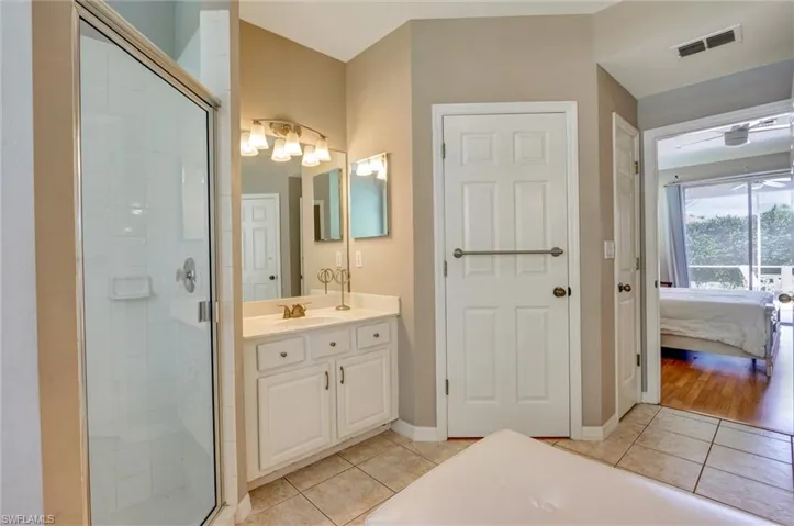 Bathroom featuring a glass-enclosed shower, single vanity with a white countertop, large mirror, and tiled flooring