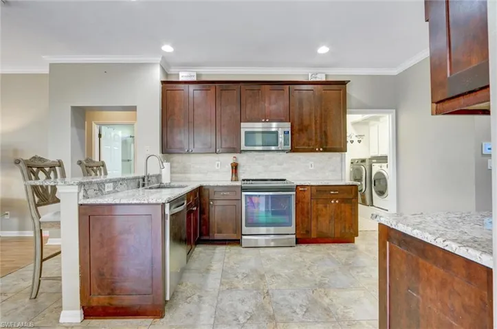 Kitchen featuring rich wood cabinetry, stainless steel appliances, light-toned stone countertops, and tile flooring