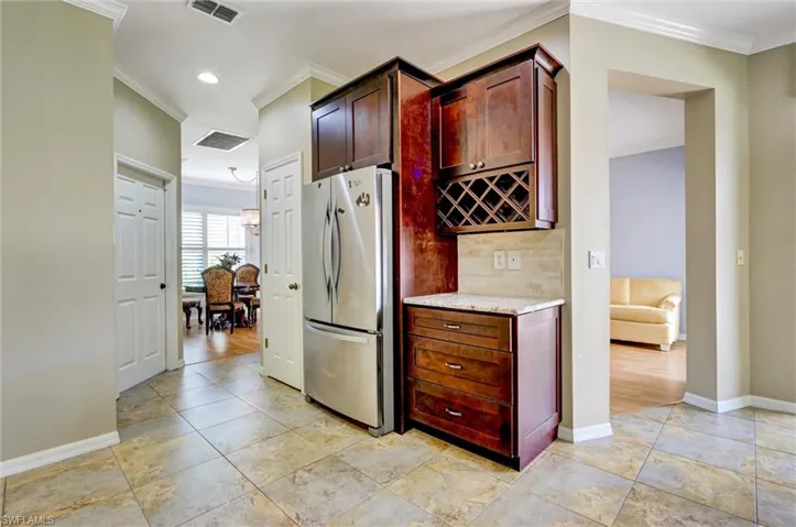 Kitchenette area featuring rich wood-finish cabinetry, built-in wine storage, a stone countertop, and a tiled backsplash