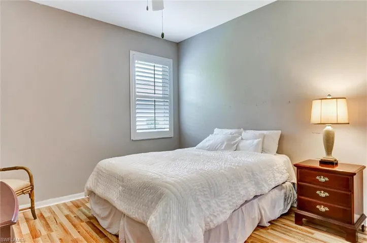 Room featuring wood-finish flooring, a window with white plantation shutters, and a ceiling fan