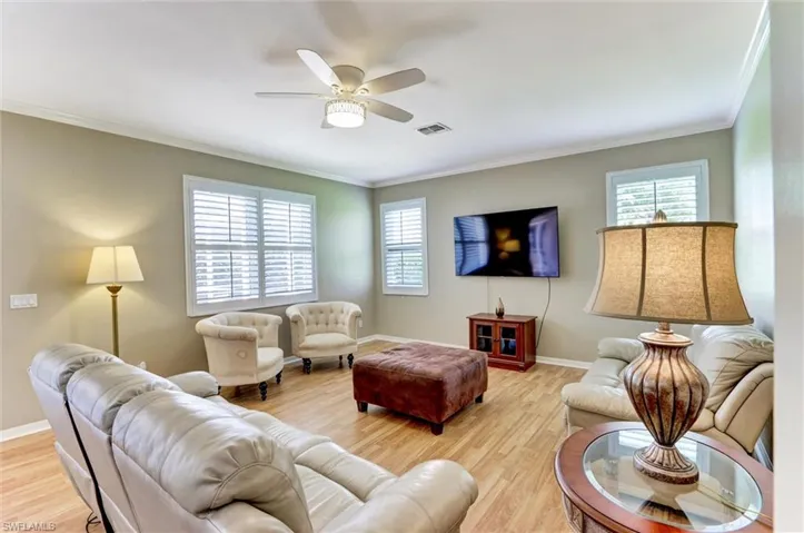 Spacious living area featuring wood-finish flooring, neutral wall tones, crown molding, and a ceiling fan with integrated lighting
