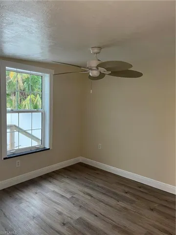Bright room featuring wood-finish flooring, an overhead ceiling fan, a window with grid inserts, and neutral wall paint