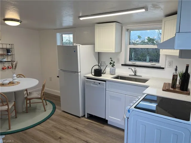 Kitchen featuring wood-finish flooring, white cabinetry, a stainless steel sink, and light-toned countertops