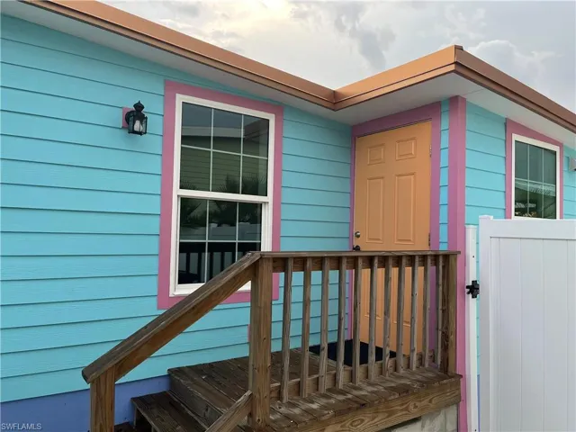 Exterior featuring vibrant blue horizontal siding with pink trim, a paneled orange front door, and a white vinyl fence