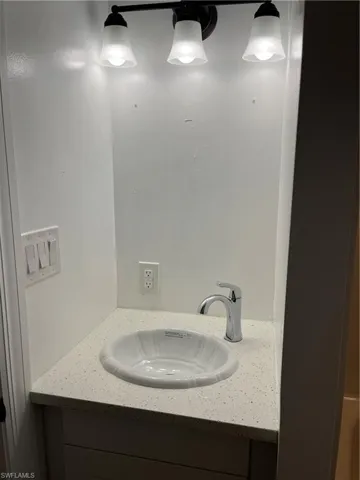 Vanity area featuring a stone-finish countertop, undermount sink, chrome faucet, and a three-light vanity fixture with frosted glass shades