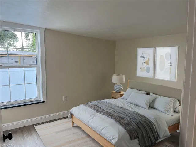 Light-filled room featuring a double-hung window with white trim, tan wall paint, and wood-finish flooring
