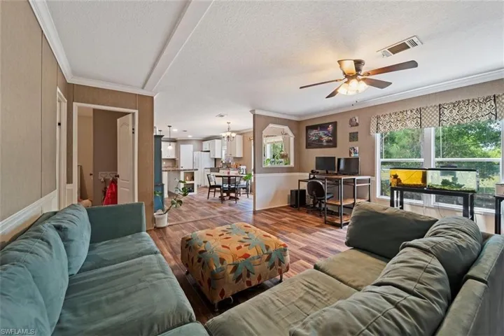 Living room with hardwood / wood-style flooring, ornamental molding, ceiling fan, and a textured ceiling