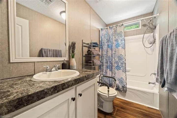 Full bathroom with a textured ceiling, shower / bath combo, hardwood / wood-style flooring, vanity with extensive cabinet space, and toilet