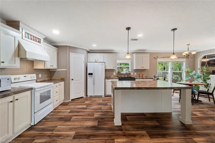 Kitchen with hanging light fixtures, a kitchen island, white appliances, dark hardwood / wood-style floors, and custom exhaust hood