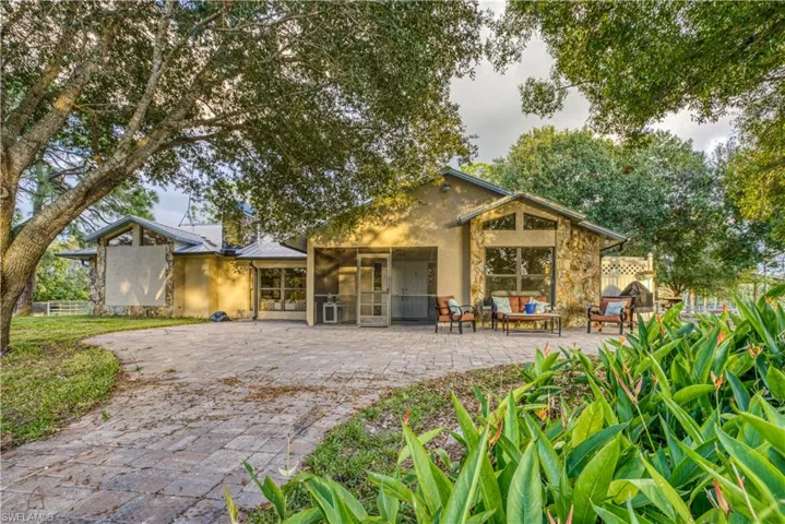 Rear view of property featuring a patio, stucco siding, and stone siding