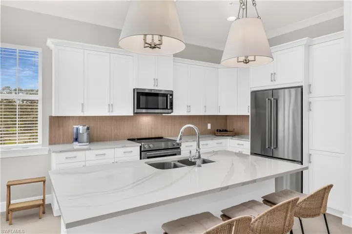 Kitchen featuring a center island with sink, white cabinets, sink, decorative light fixtures, and stainless steel appliances