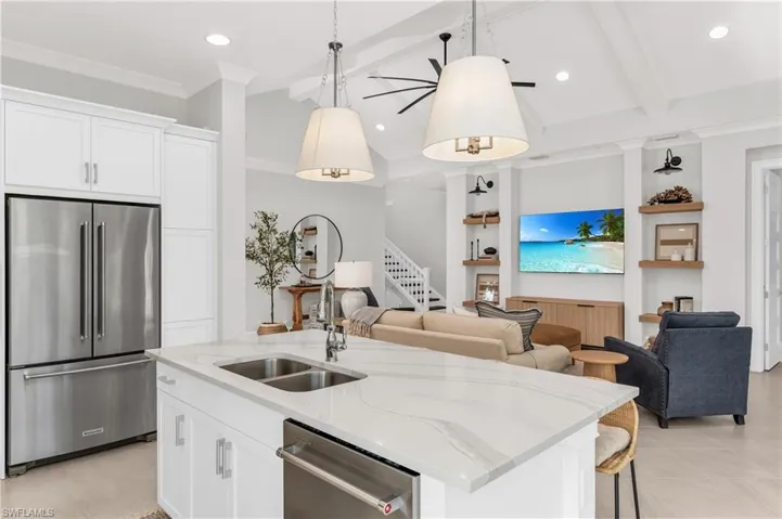 Kitchen featuring light stone counters, stainless steel appliances, white cabinets, hanging light fixtures, and an island with sink