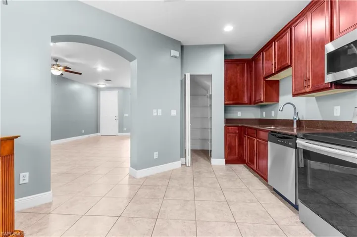 Kitchen with ceiling fan, sink, stainless steel appliances, dark stone counters, and light tile patterned flooring