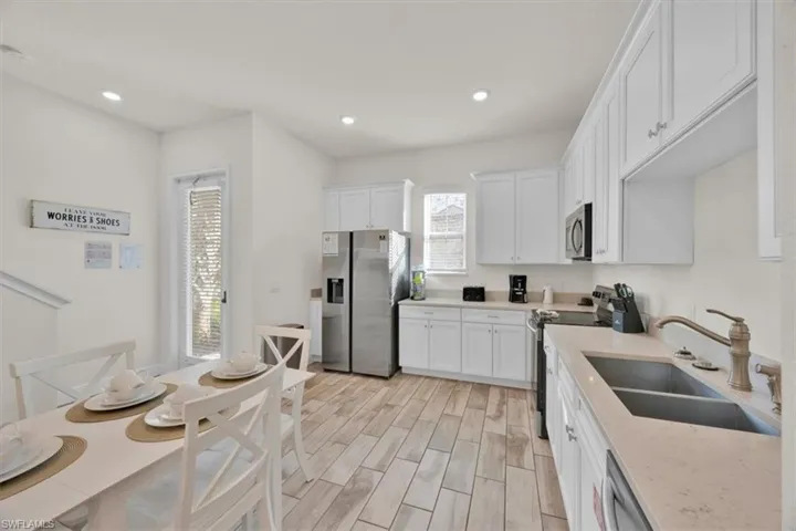 Kitchen featuring white cabinets, stainless steel appliances, wood tiled floors, light stone counters, and recessed lighting