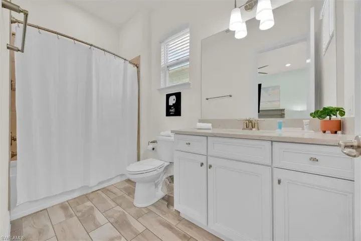 Full bathroom featuring shower / bath combo with shower curtain, vanity, wood tiled floors, and hanging lights