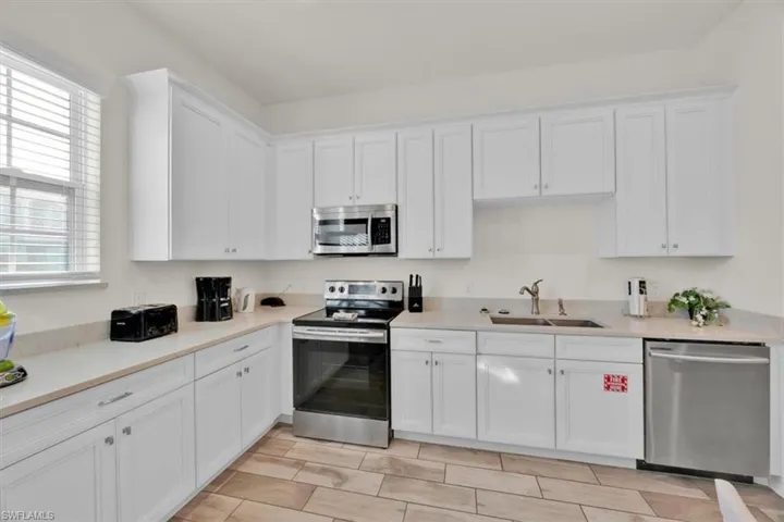 Kitchen with stainless steel appliances, white cabinets, and light stone counters