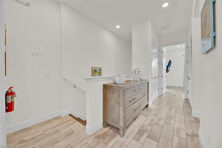 Hall with an upstairs landing, wood finish floors, and recessed lighting