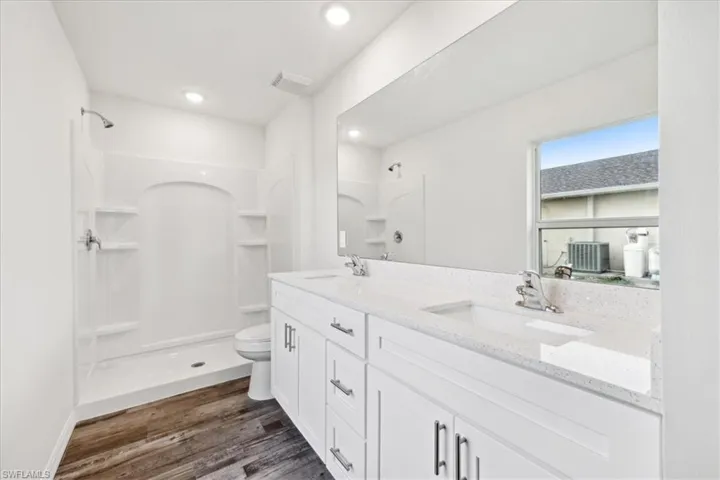 Bathroom with hardwood / wood-style floors, walk in shower, toilet, and vanity