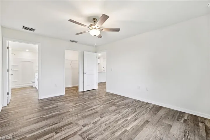 Unfurnished bedroom featuring ceiling fan, hardwood / wood-style flooring, a spacious closet, and ensuite bath