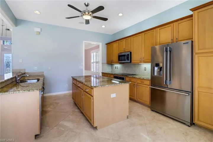 Kitchen with ceiling fan, light tile patterned floors, granite countertops, and an island.