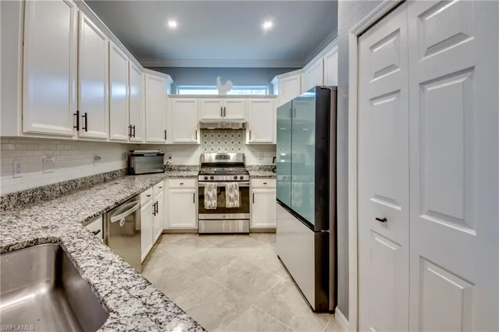 Kitchen featuring light stone countertops, light tile patterned floors, ornamental molding, white cabinetry, and stainless steel appliances