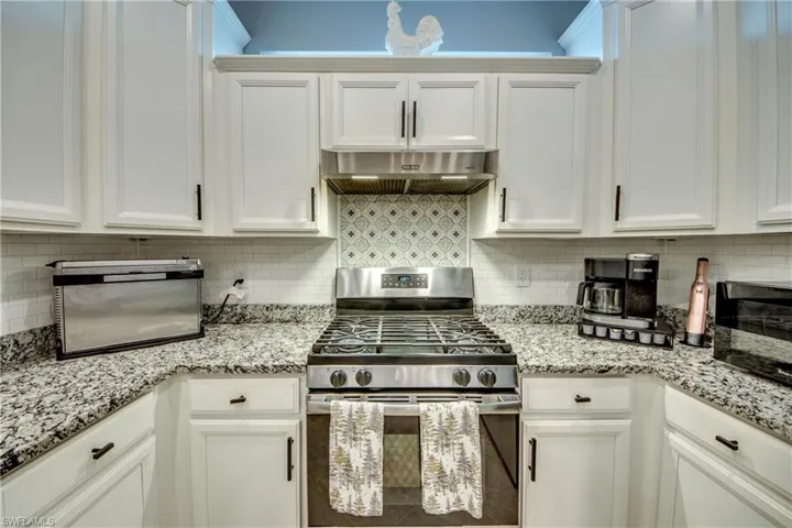 Kitchen with white cabinets, decorative backsplash, stainless steel range with gas cooktop, and exhaust hood
