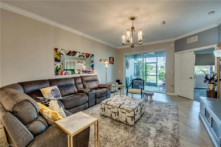 Living room with light tile patterned floors, crown molding, and an inviting chandelier