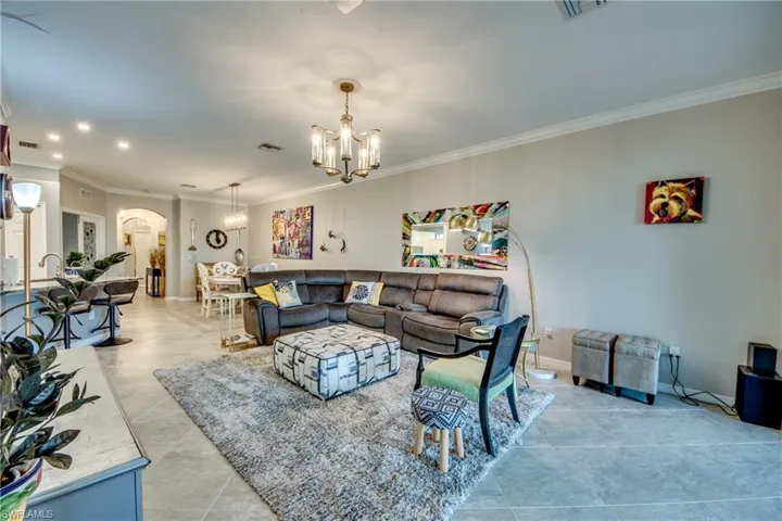 Living room with light tile patterned floors, an inviting chandelier, and ornamental molding
