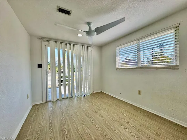 Empty room featuring light wood finished floors, a ceiling fan, a textured ceiling, and a textured wall