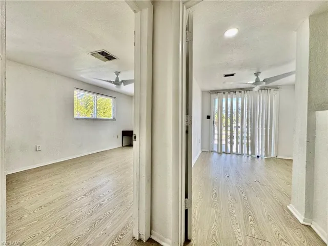 Hall featuring a textured ceiling, a textured wall, and light wood finished floors