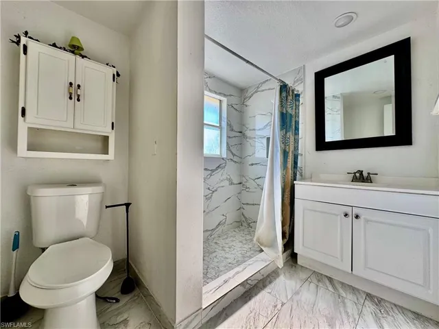 Bathroom featuring a marble finish shower, vanity, light marble finish flooring, and a textured ceiling