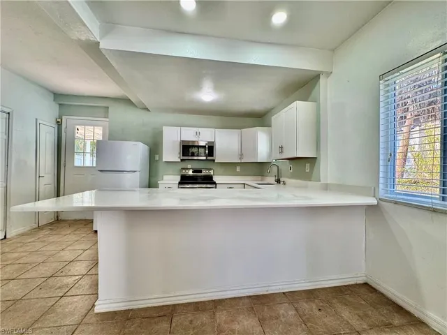 Kitchen featuring white cabinets, stainless steel appliances, light stone counters, a peninsula, and a breakfast bar
